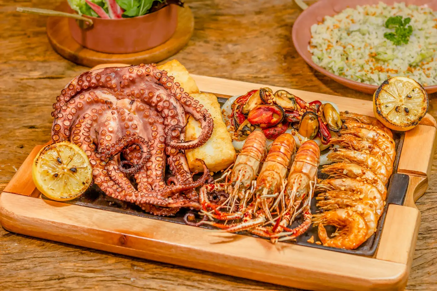 Pulpo y langostinos a la parrilla sobre una tabla de madera, con limón y arroz
